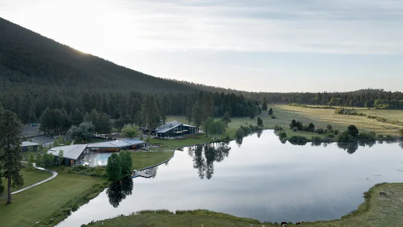 Aerial view of the buildings beside a calm lake reflecting the forested hillside at dawn