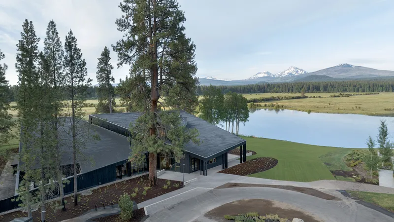 Elevated view of the sloped metal roof volumes nestled among pines with snowcapped mountains in the distance