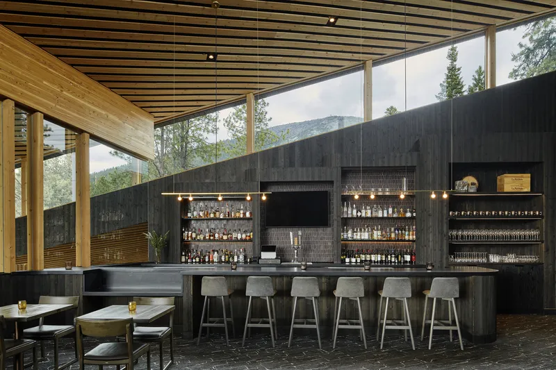 Bar area with dark tile-clad backdrop displaying bottles and tap system beneath a slatted timber ceiling and clerestory glazing