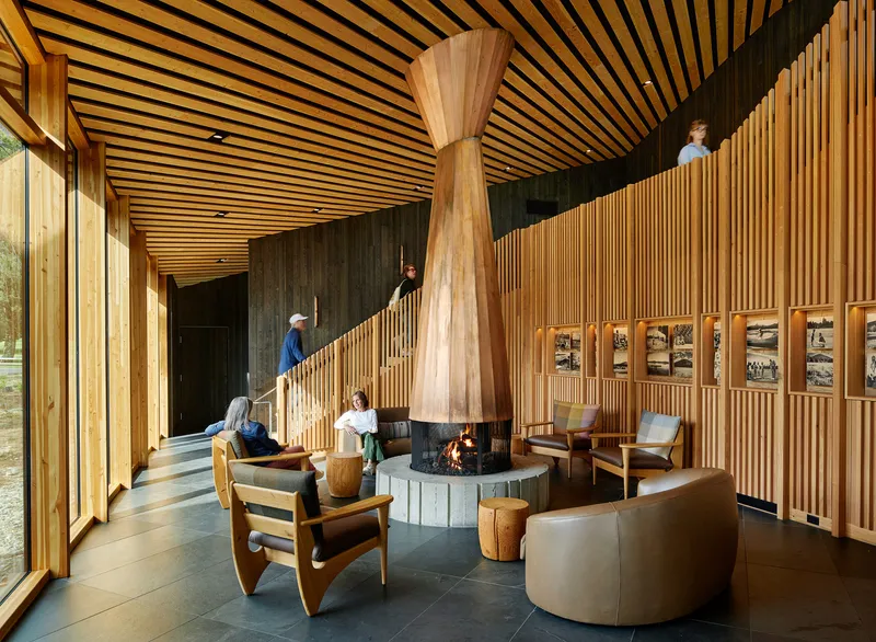 Lobby with central sculptural fireplace column and visitors ascending vertical slat-clad staircase