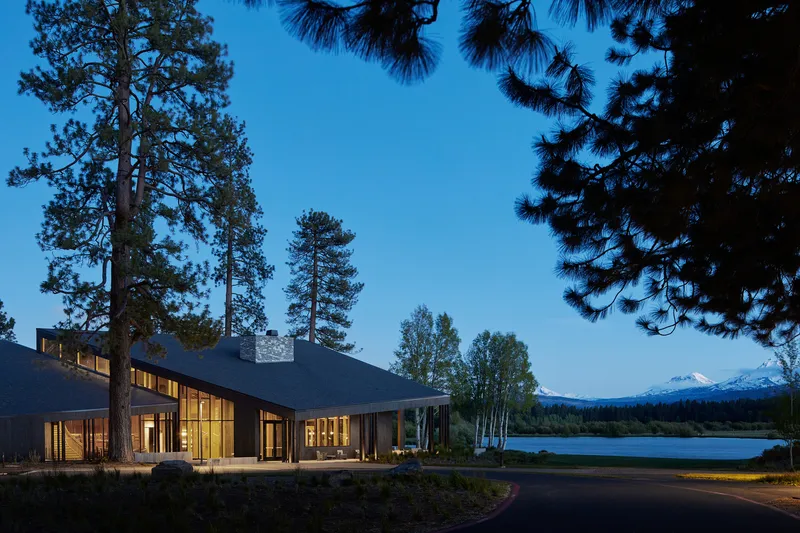 Lakeside facade with floor-to-ceiling glazing and exposed timber structure at twilight beneath tall pines