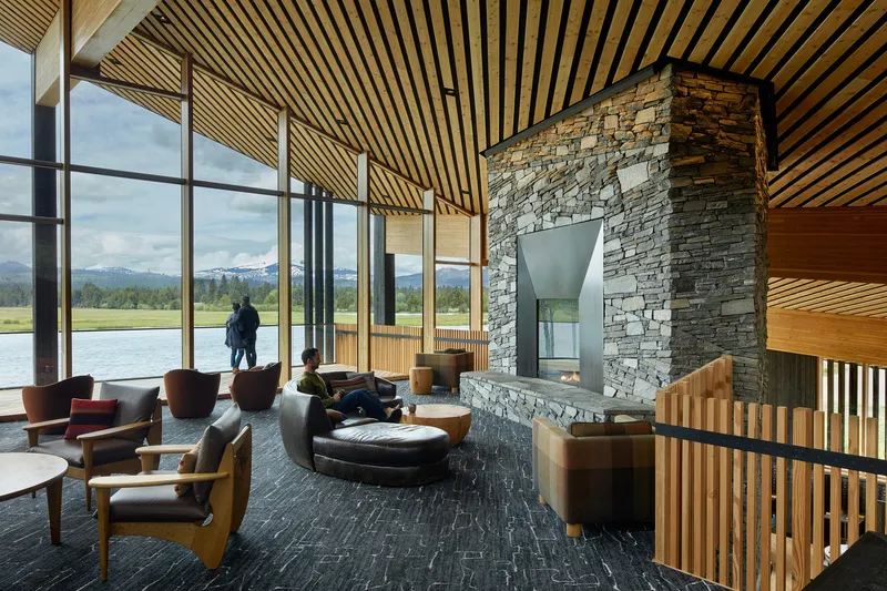 Lounge area with layered stone fireplace surround beneath angled timber slat ceiling planes