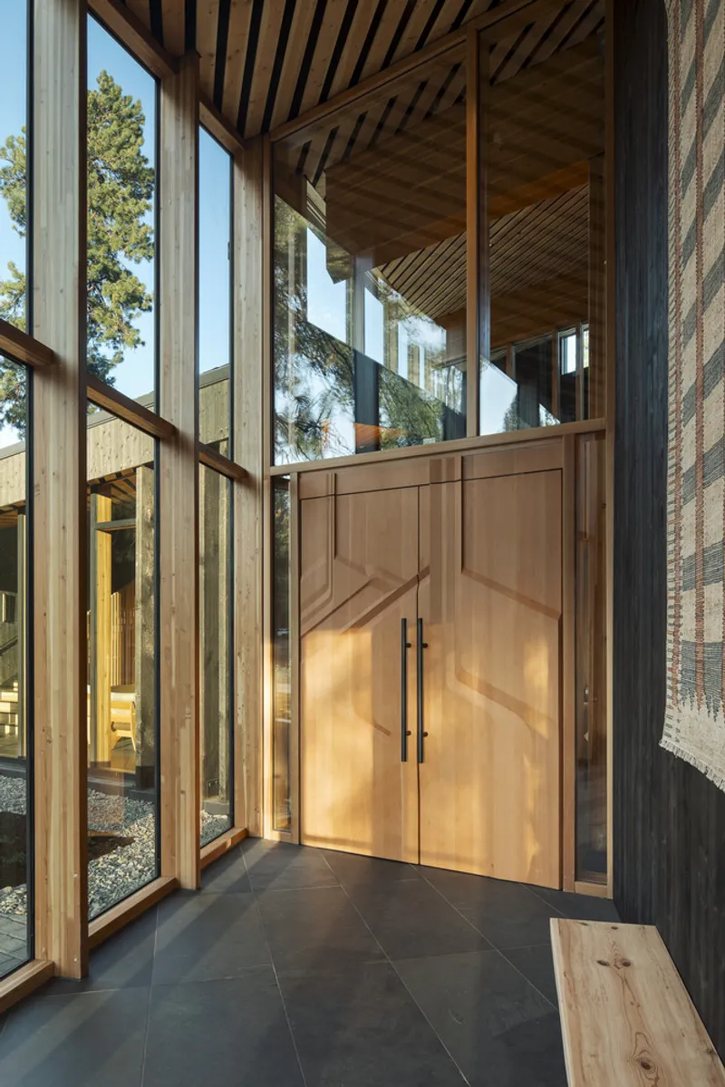 Glass-enclosed entry vestibule with paired timber doors, slatted wood ceiling and dark tile flooring