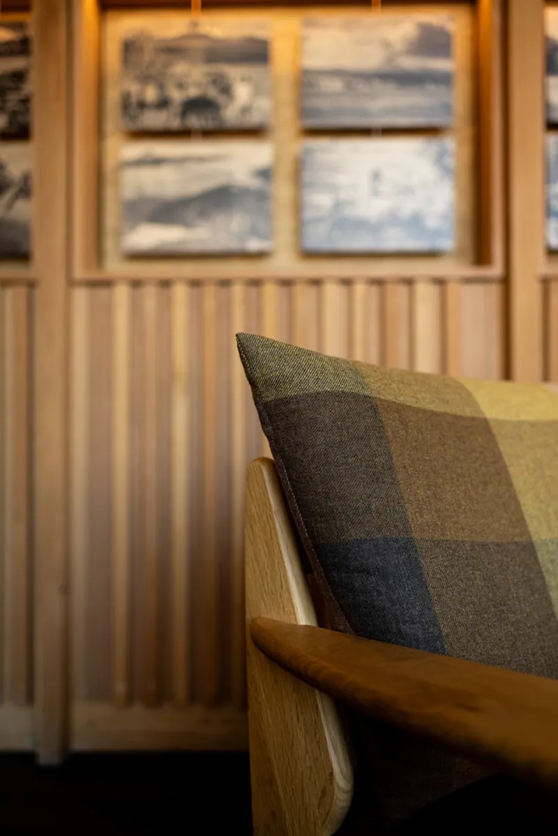 Close-up of an oak bench with a checkered wool cushion against vertical timber slat wainscoting