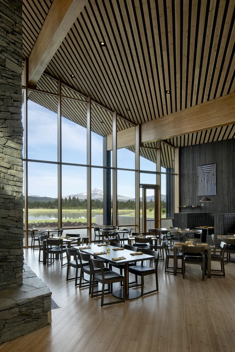 Dining room with slatted timber ceiling and floor-to-ceiling windows overlooking a wetland meadow