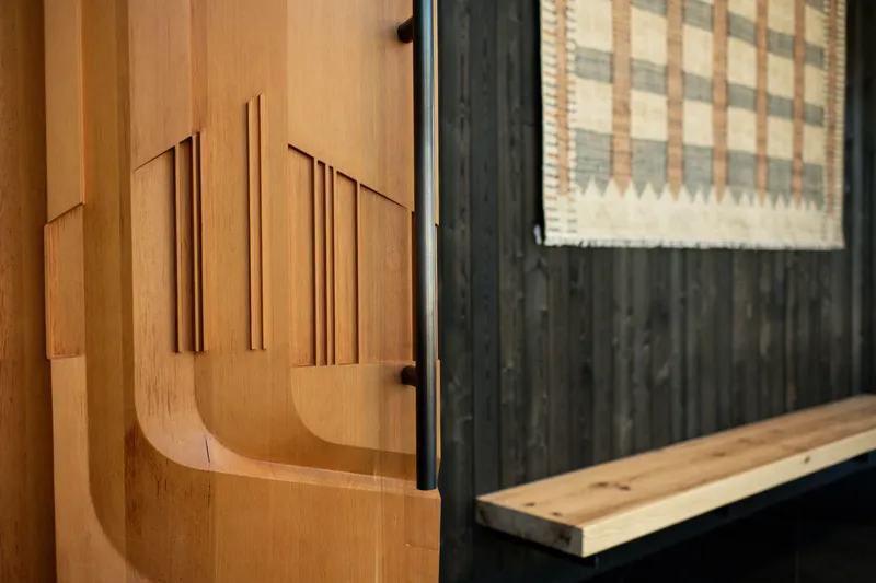 Relief-carved timber wall panel with geometric motifs next to a darkened timber door frame