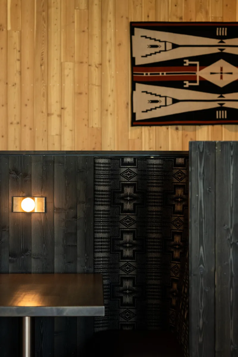 Detail of charred timber wall panels with mounted sconce beside patterned textile hangings