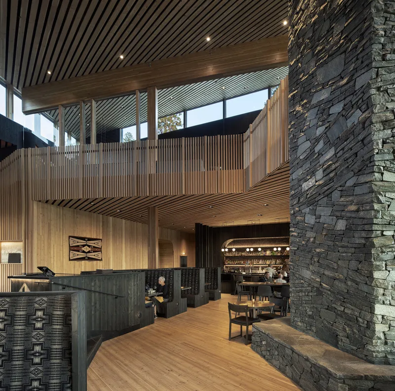 Double-height lobby with timber slat ceiling, stone fireplace and upper mezzanine balcony