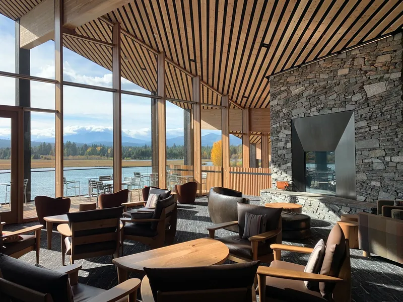 Double-height lounge with stone fireplace wall, slatted timber ceiling and views to the lake and mountains