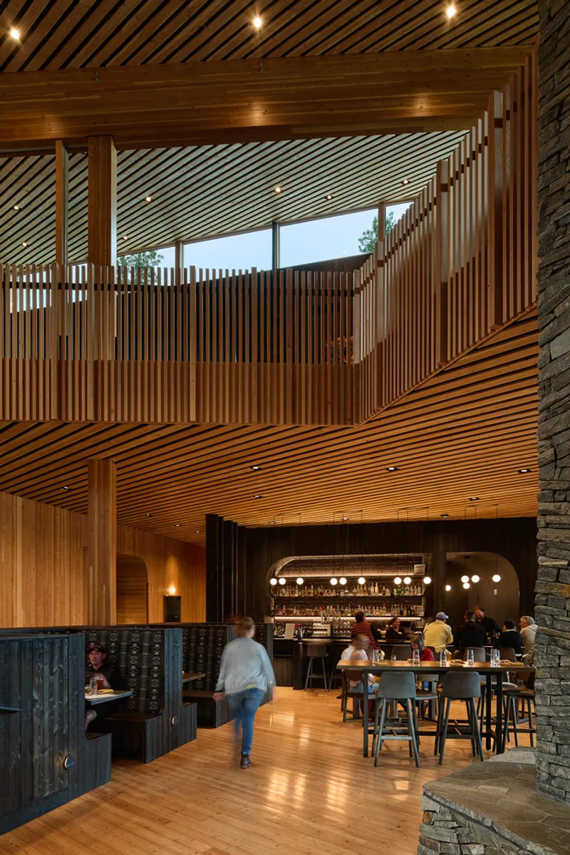 Double-height interior showing timber slatted mezzanine screen above the bar with diners on the floor below
