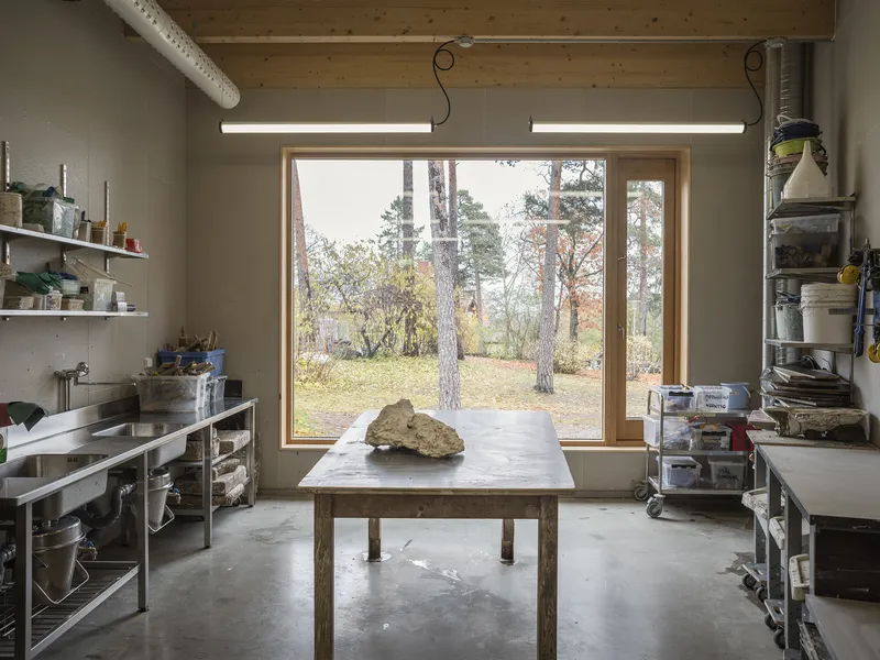Studio space with a timber-framed window opening onto a forested landscape with pine trees