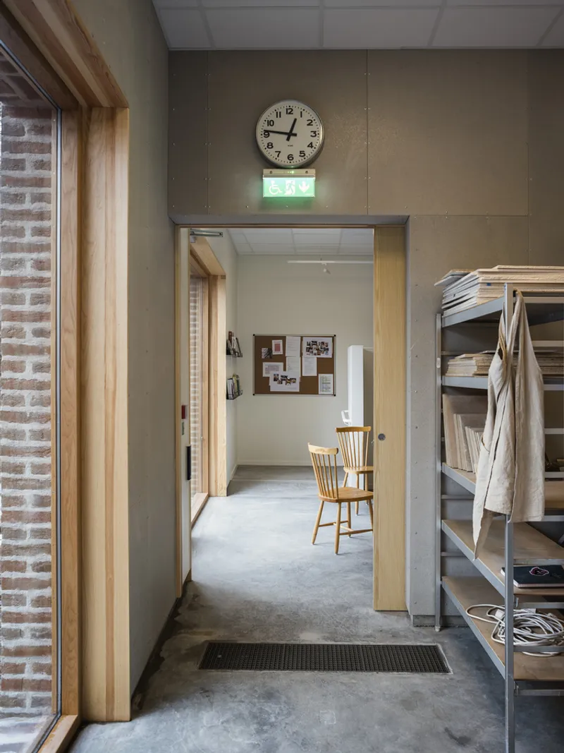 Interior doorway sequence with concrete walls, timber frames and a clock above the passage