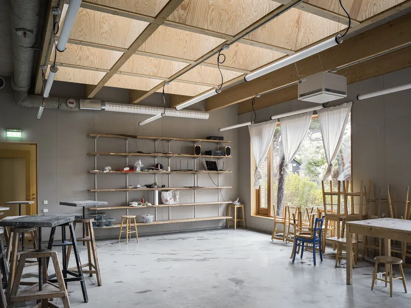 Workshop interior with exposed plywood ceiling panels, concrete floor and open shelving near a curtained window
