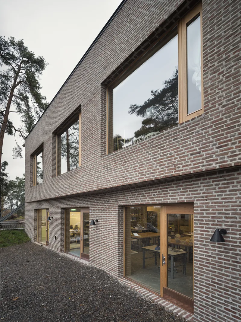 Two-story brick facade with timber-framed windows and glazed doors opening to gravel courtyard at dusk
