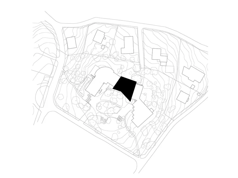 Site plan drawing showing building footprint highlighted in black among landscaped grounds and neighboring structures