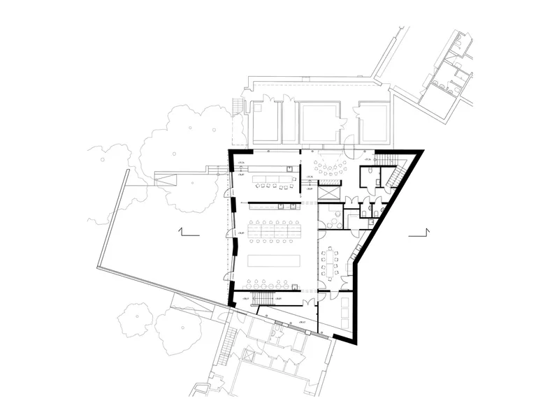 Ground floor plan drawing with angular geometry, open workspaces, service rooms, and adjacent tree canopies