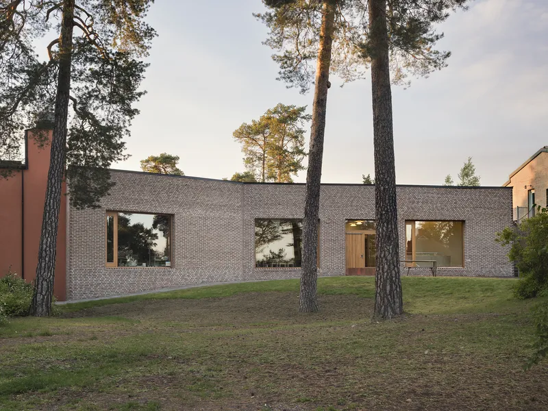 Grey brick facade with timber-framed windows among tall pine trees at dusk