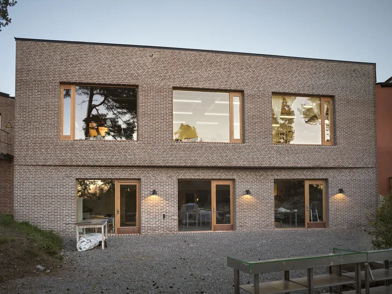 Two-storey brick elevation with timber-framed openings and exterior lighting at twilight