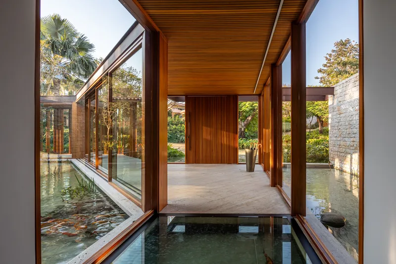 Covered walkway with timber ceiling and columns spanning a shallow reflecting pool on both sides