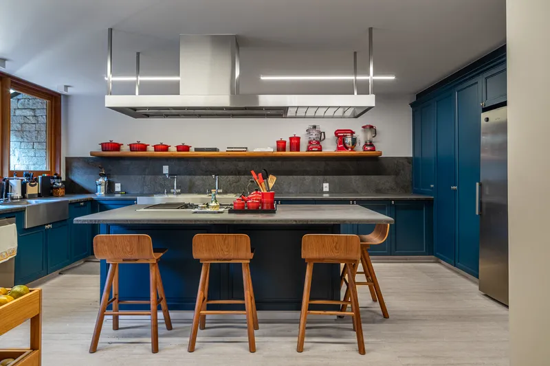 Kitchen island with dark countertop and wooden stools beneath a stainless steel range hood