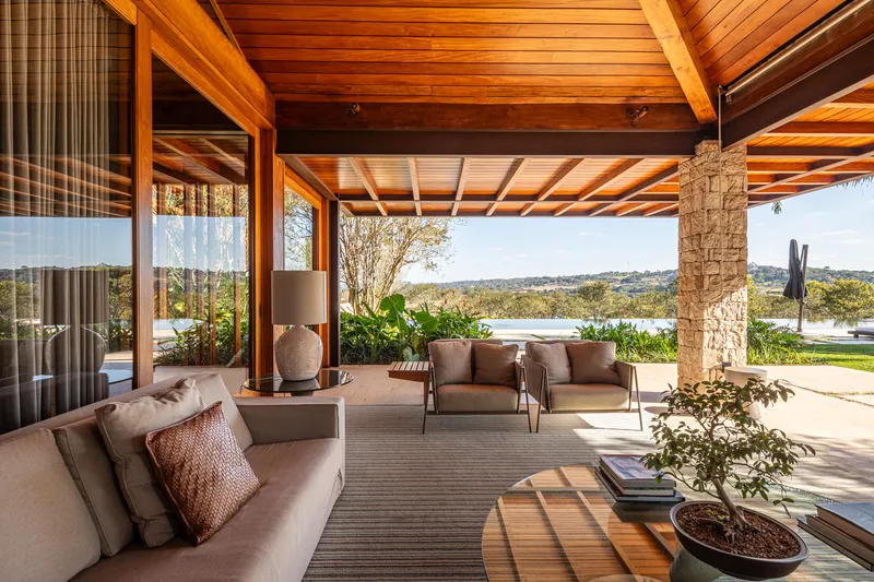 Open living area beneath timber ceiling with stone column and views to lawn and water beyond