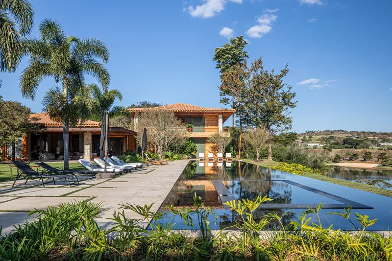 Pool terrace overlooking a lake with the two-story timber and stone facade under midday sun