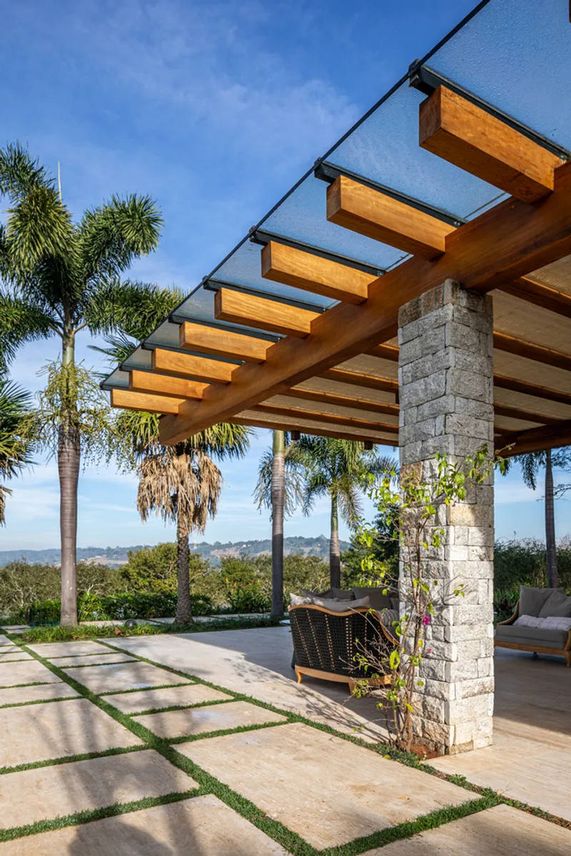 Covered pavilion with timber beam pergola, stone pillars and grass-jointed paving beneath palm trees