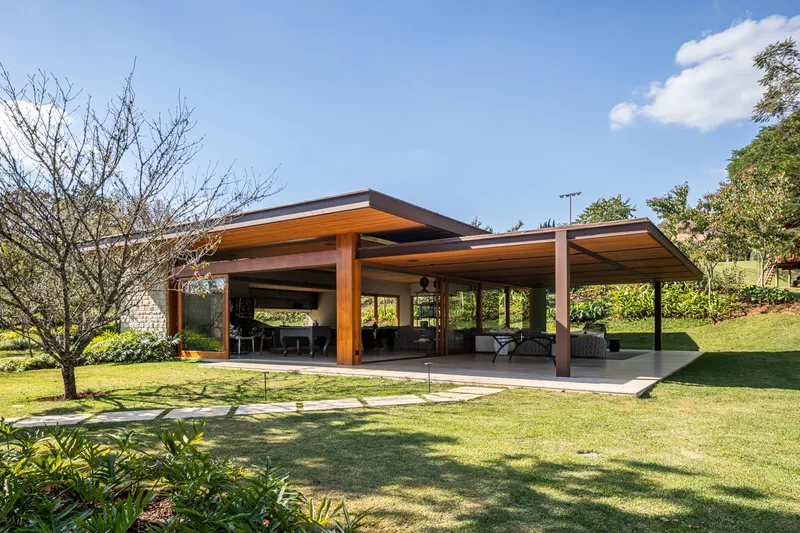 Open-sided pavilion with timber columns and flat roof cantilevering over a lawn with deciduous trees