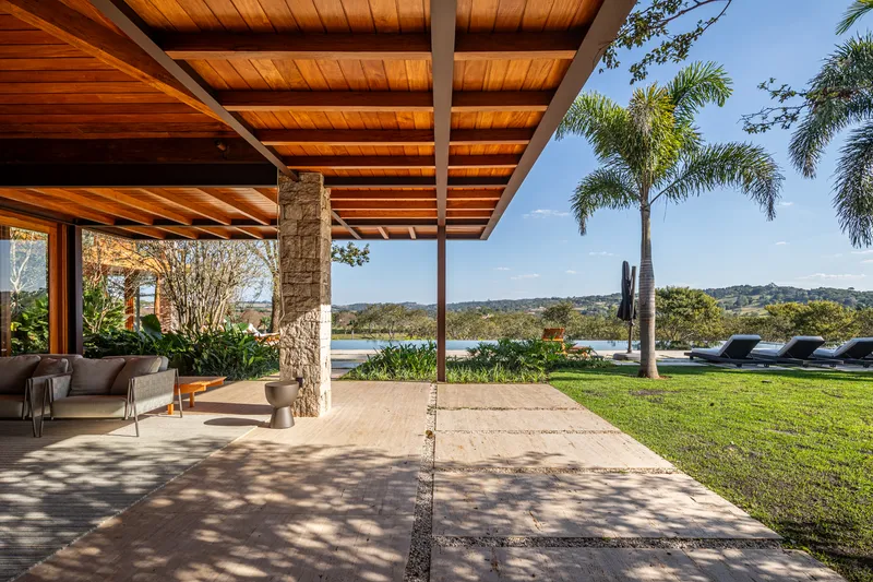 Covered terrace with exposed timber beams and stone column overlooking lawn and distant lake under palm trees