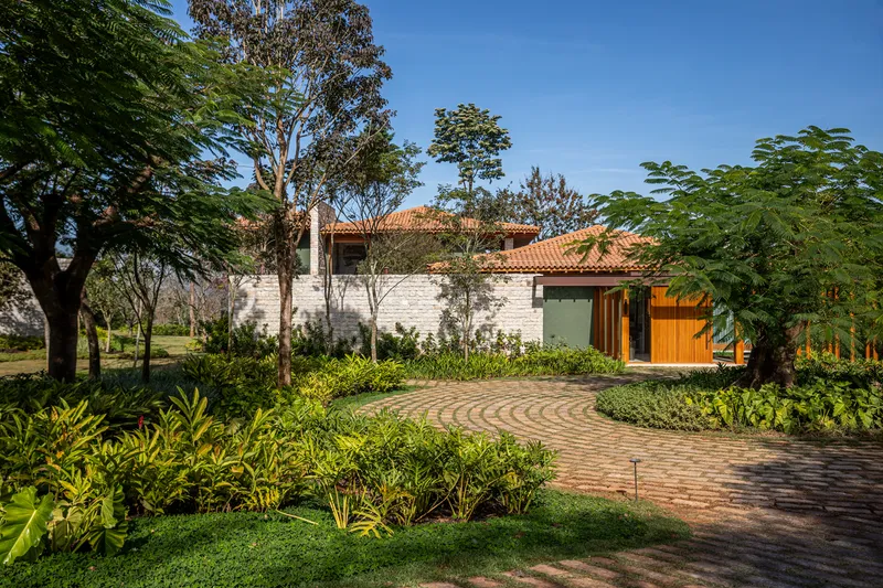 Curved brick driveway leading through planted beds to a tile-roofed residence framed by mature trees