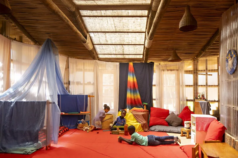 Interior activity room with woven reed skylight panels, timber structure, and children gathered on red floor cushions