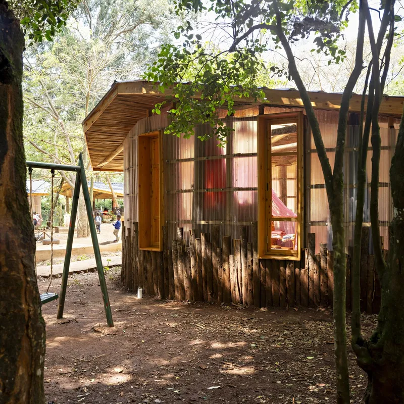 Timber pavilion with corrugated metal walls and vertical log cladding surrounded by trees and forest floor