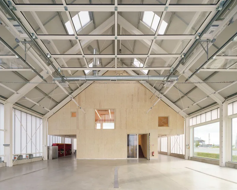 Plywood gabled training structure within large garage space with steel truss roof and skylights
