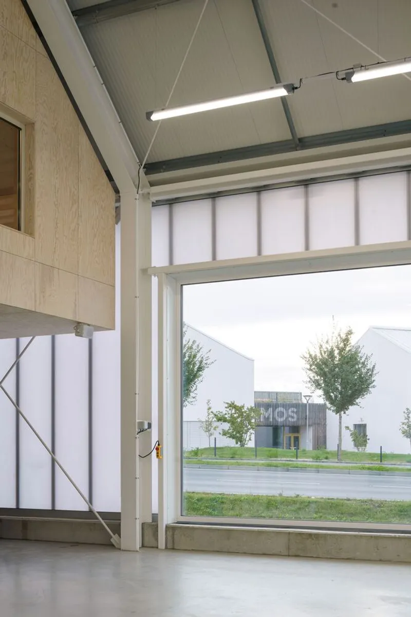 Interior view through a large garage door opening to the street with young trees outside