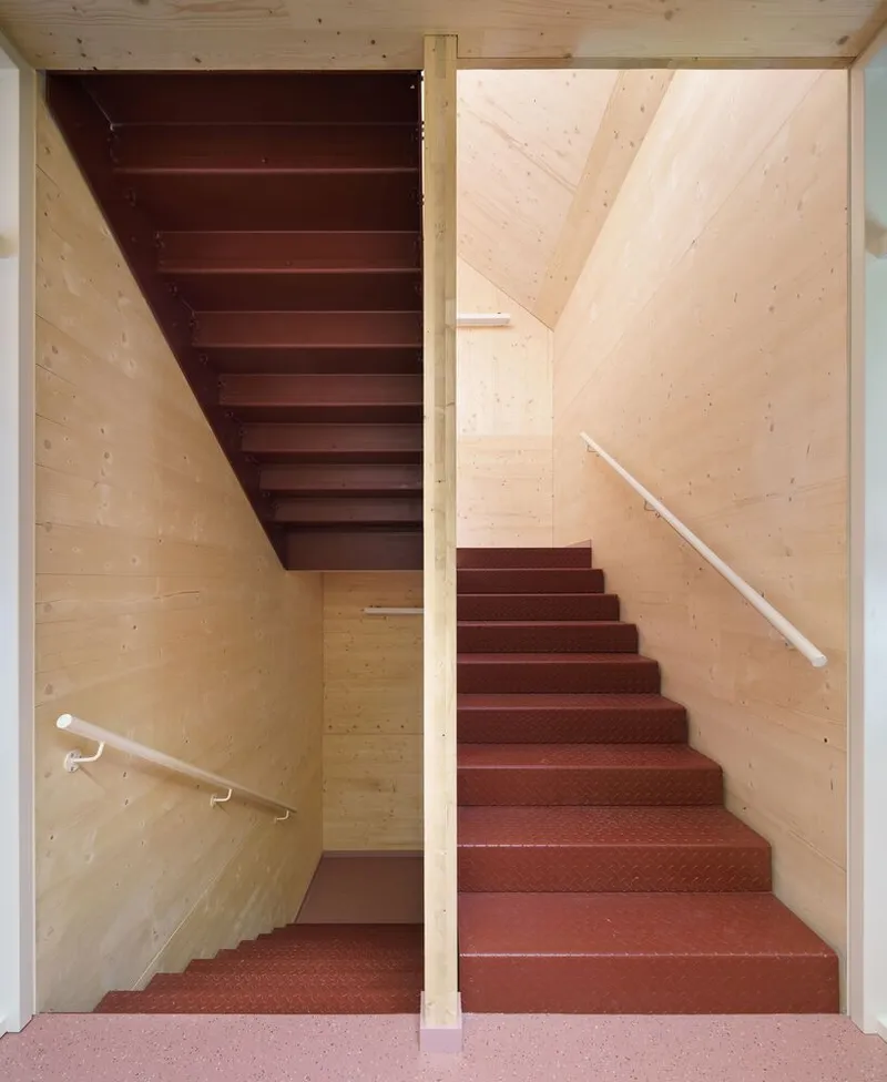 Switchback staircase with red rubber treads and pale timber wall panels under a skylight