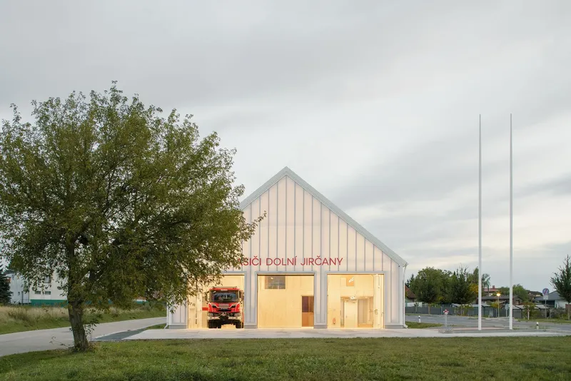 Front elevation of the gabled fire station with illuminated bays under an overcast sky