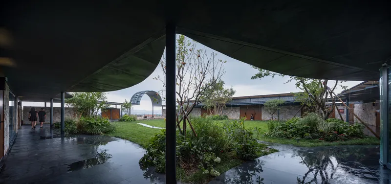 Covered walkway overlooking a central courtyard with planted beds and reflecting pools after rain