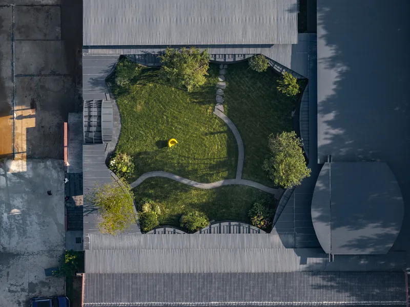 Aerial view of the three-lobed courtyard with curved pathways and lawn surrounded by concrete and metal roofs
