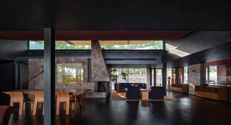 Open-plan living space with stone fireplace, timber beams, and clerestory windows framing trees outside
