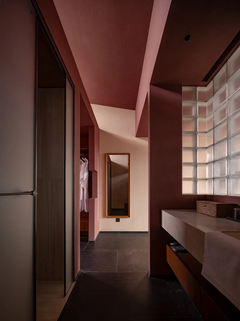 Bathroom corridor with terracotta-painted ceiling, glass block wall, and concrete vanity counter