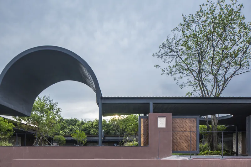 Curved metal canopy entry with timber gate panels set in a pink stucco perimeter wall