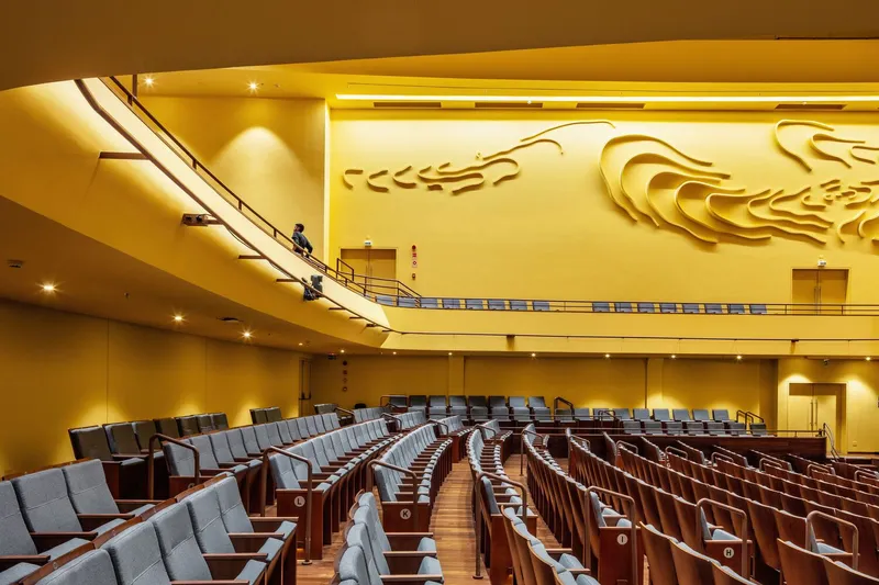 Interior view of the auditorium showing curved balcony rail and relief sculpture on the gold-toned back wall