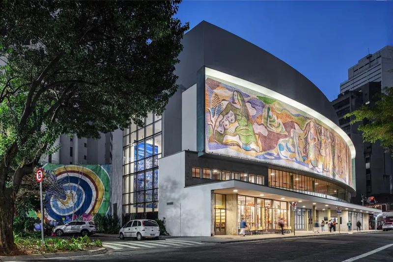 Corner view of the curved facade with mosaic mural illuminated at twilight beneath a blue sky