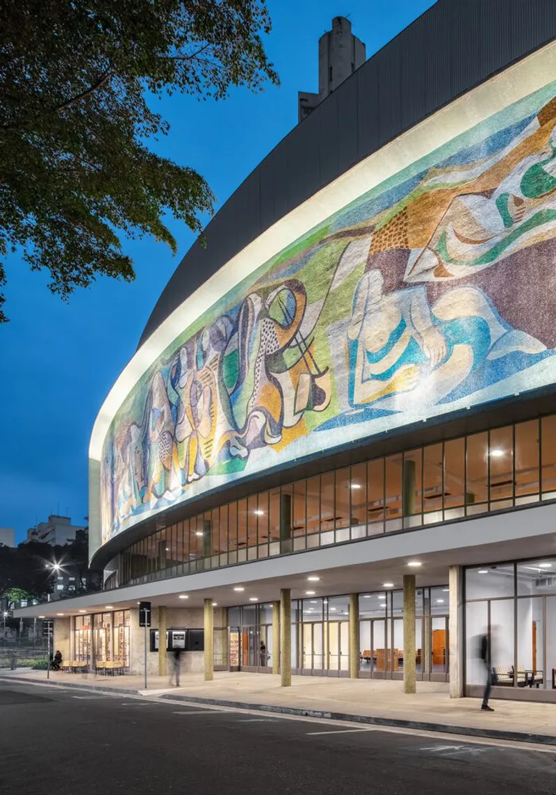 Close-up of the curved facade showing the mosaic frieze above the glazed colonnade at dusk