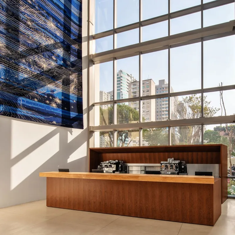 Timber service counter beneath a tall window wall with reflective metal artwork and afternoon light