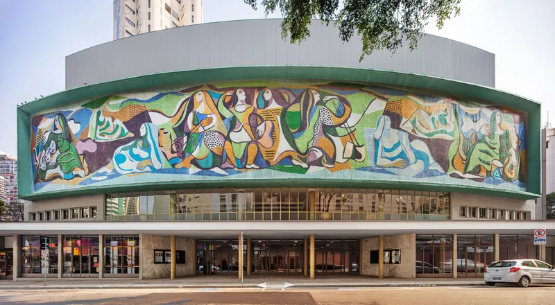 Street view of the curved building with panoramic mural and glazed colonnade at ground level