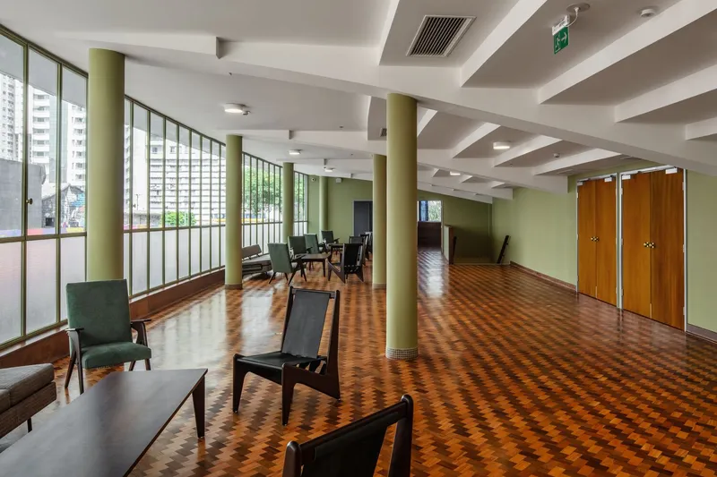 Interior lounge with green cylindrical columns, parquet flooring and gridded window wall overlooking the city
