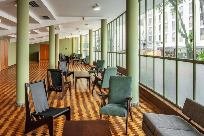 Long interior hall with green columns, patterned parquet and modular seating beneath coffered ceiling beams