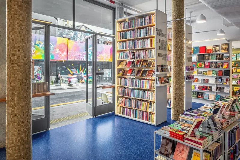 Bookstore interior with blue rubber flooring, cork-clad columns and glazed storefront opening to pedestrian plaza