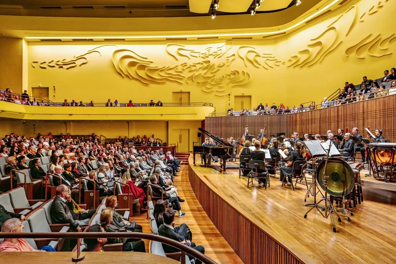 Orchestra performing on timber stage before audience seated in main floor and curved balconies